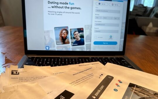 A lap top sits open on a dining table. The screen shows photos of two people. There are papers on the table.